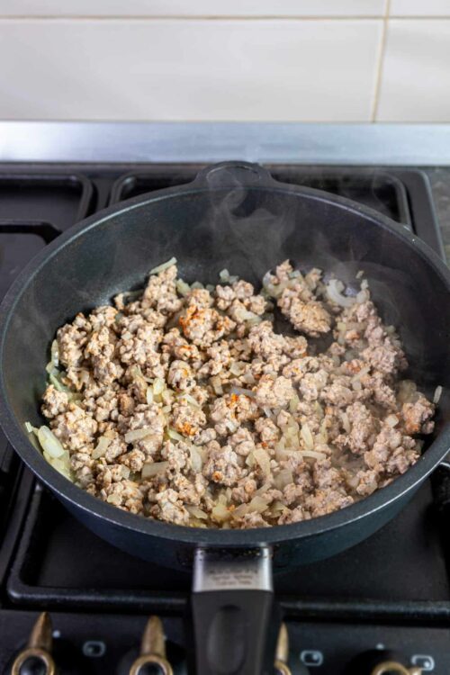 Cooked ground beef with onions in a skillet for Spanish beef picadillo recipe.