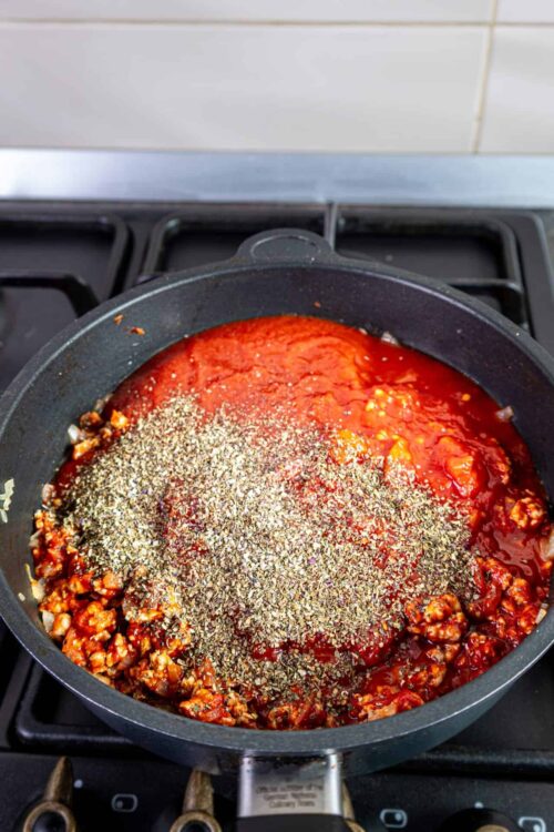 Rich tomato sauce with herbs simmering in a skillet on stovetop.