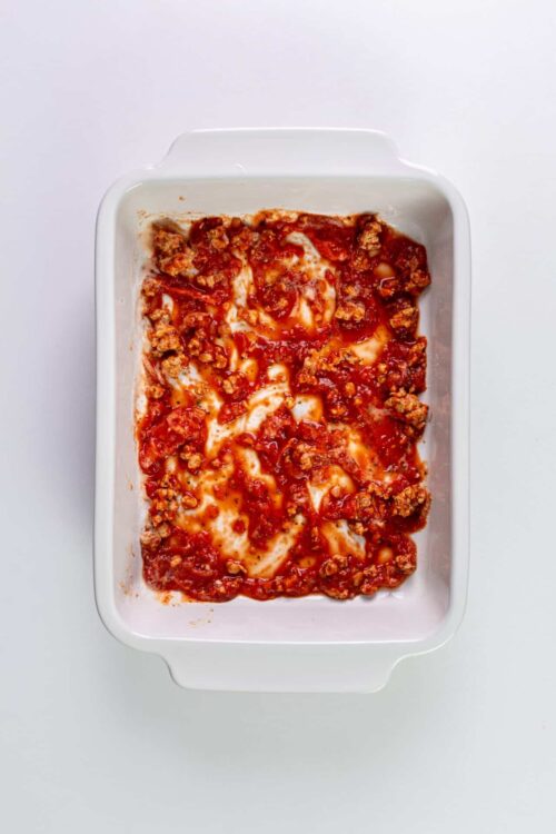 Cheesy baked lasagna with ground meat and tomato sauce in a white casserole dish.