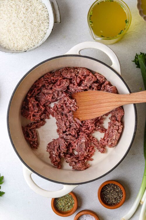 Minced raw beef in a skillet with herbs and seasonings for cooking recipes.