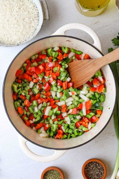 Diced green, red, and white vegetables in a white cast iron skillet for cooking.