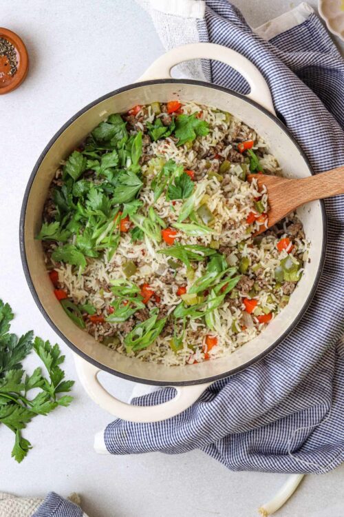 Creamy beef and rice skillet with fresh herbs and vegetables in a white casserole dish.