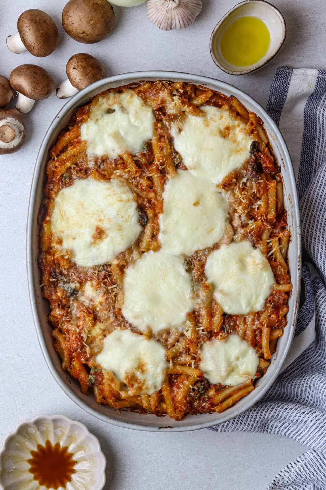 Cheesy baked ziti casserole with melted mozzarella and tomato sauce in an oval baking dish on a white countertop.
