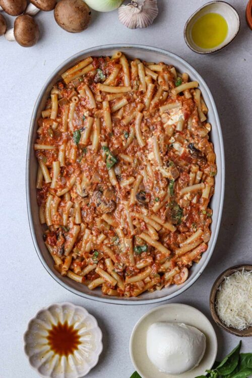 Savory baked pasta casserole with tomato sauce, cheese, and herbs on white ceramic dish.