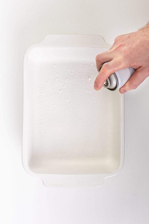 Aerosol spray can being used on a white baking dish to create a non-stick surface.