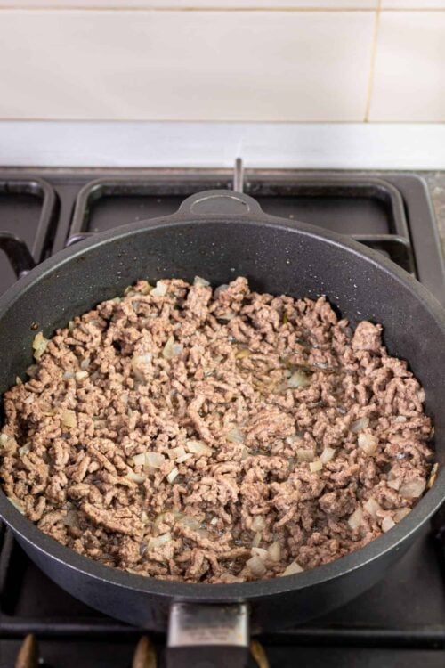 Ground beef cooking in a skillet with chopped onions on a stovetop.