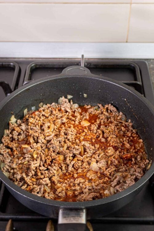 Ground beef and onions cooking in a black skillet on a stovetop.