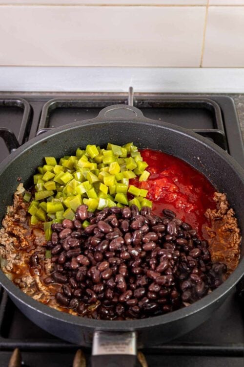 Cilantro, beef, tomato, and black bean chili cooking in a skillet on stovetop.