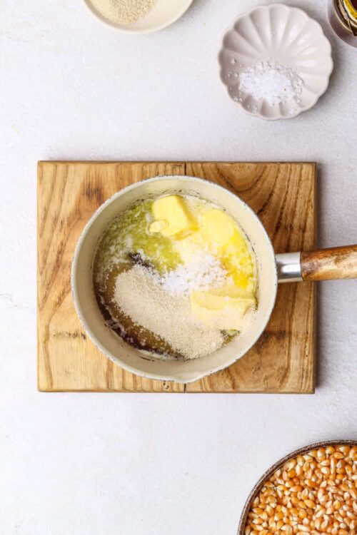 Cream melting with butter and cheese in a saucepan on wooden cutting board.