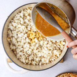 Buttered popcorn in a large skillet with melted butter being poured over it.