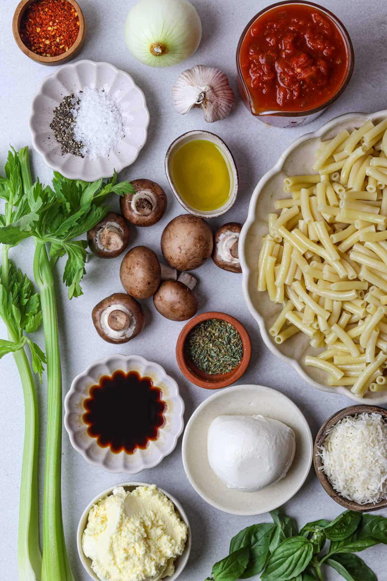 Fresh ingredients for baked pasta dish, including mushrooms, pasta, garlic, herbs, and tomato sauce.