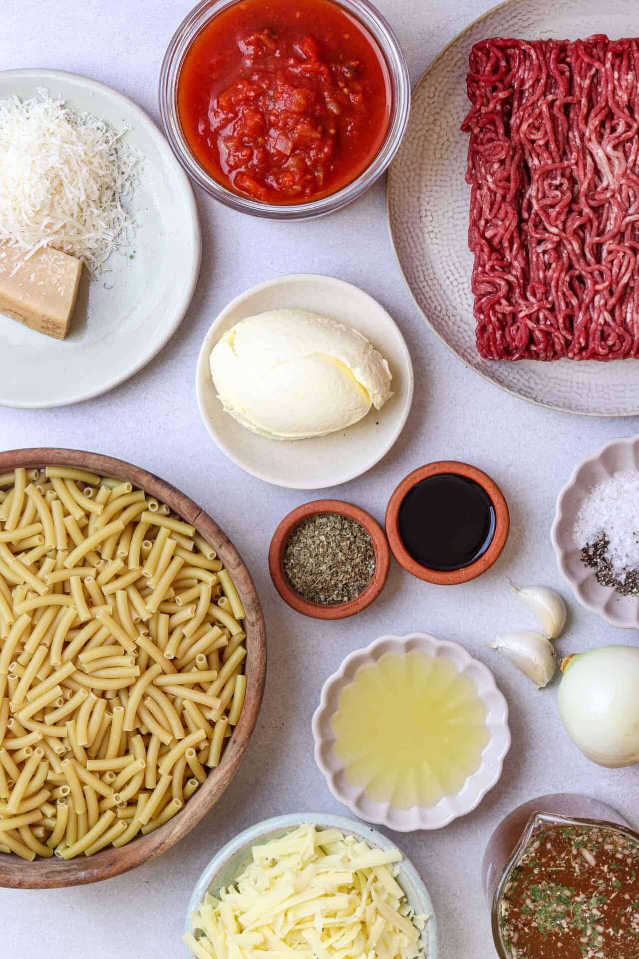 Ground beef and pasta ingredients for baked ziti, including cheese, tomato sauce, and seasonings.