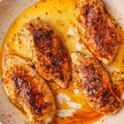 Juicy, seasoned chicken breasts cooking in a skillet with flavorful spices and butter.