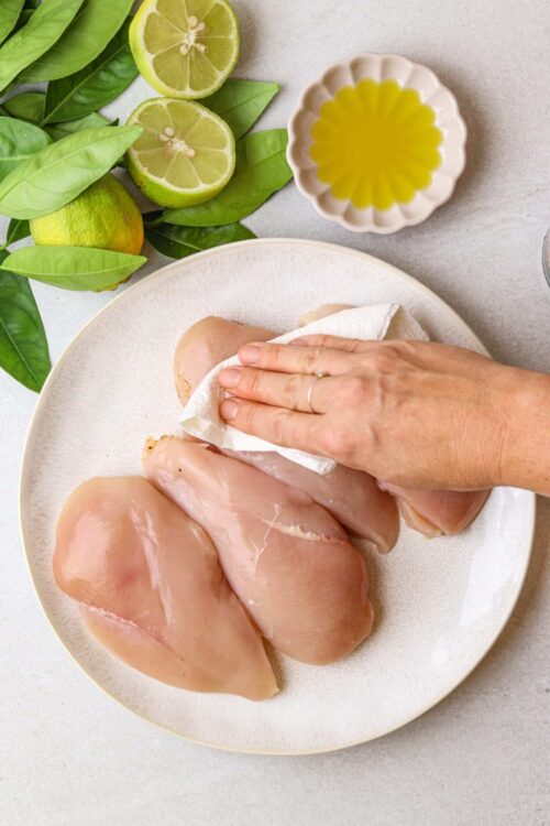Fresh raw chicken breasts on a plate with lemon and basil.