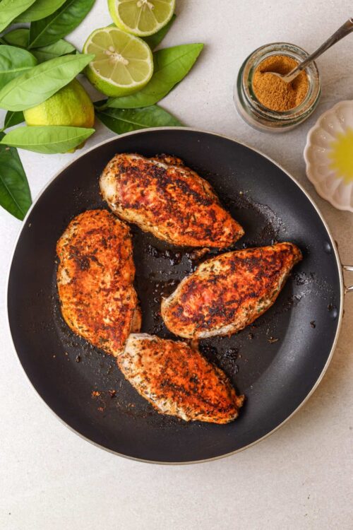 Juicy grilled chicken breasts with spices in a black skillet.