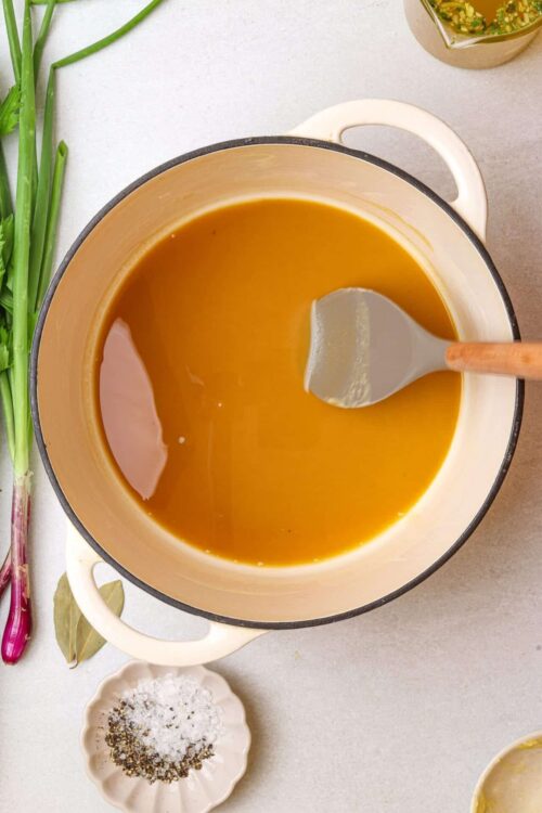 Golden caramel sauce in a pot with a silicone spatula on a neutral background.