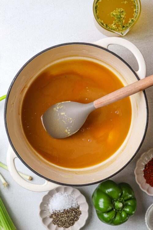 Creamy butternut squash soup in a pot with a ladle, surrounded by fresh vegetables and seasonings.