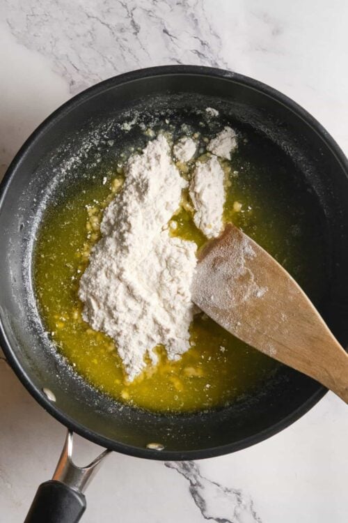 Flour being added to melted butter in a black skillet for baking recipes.
