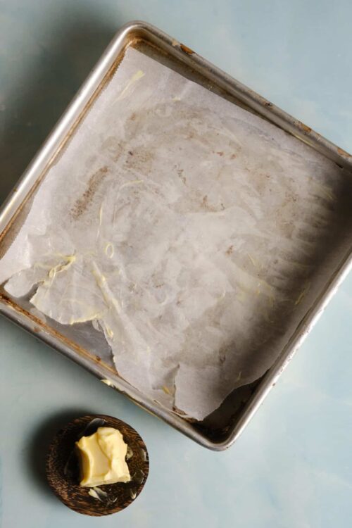 Ungreased baking sheet with parchment paper and a small dish of butter for baking.