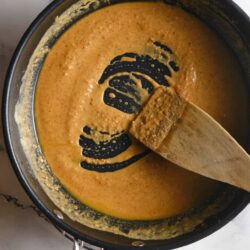 Creamy homemade butternut squash soup cooking in a black saucepan on a marble countertop.