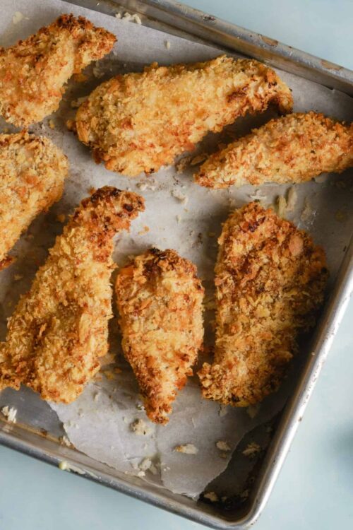Crispy baked chicken tenders with golden breadcrumb coating on a baking sheet.