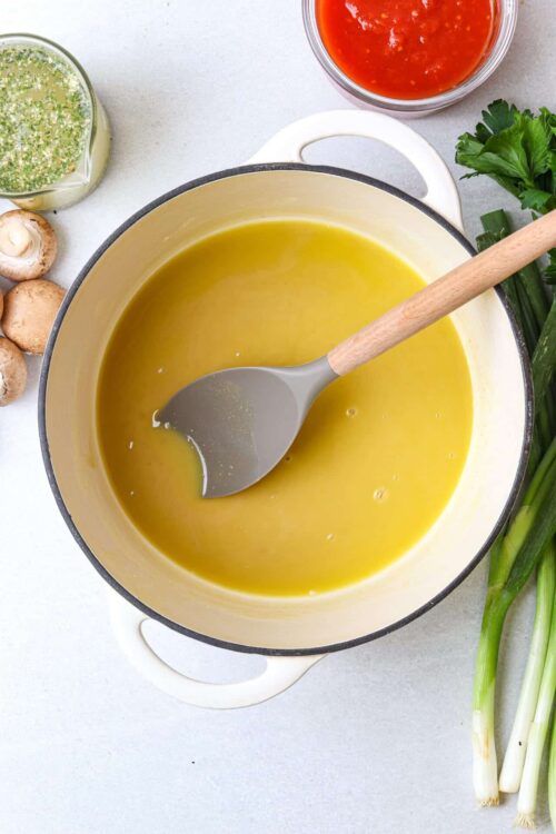 Creamy herb and vegetable soup with fresh ingredients on a kitchen countertop.
