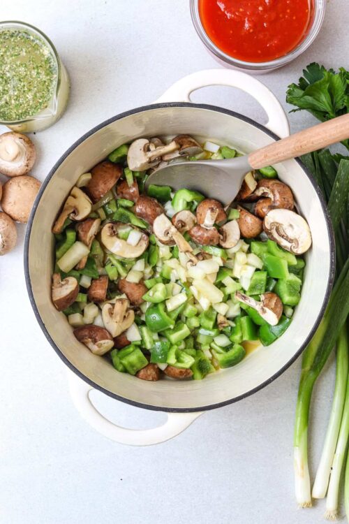 Sautéed mushrooms and celery in a white skillet with green onions and fresh herbs on the side.
