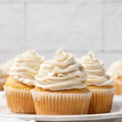 Vanilla cupcakes with creamy frosting on a white plate.