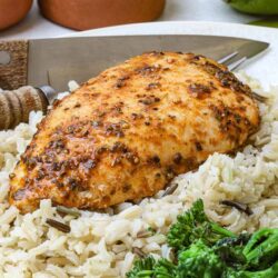 Juicy baked chicken breast with herbs on rice and broccoli, healthy dinner idea.