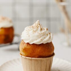 Cream-filled cupcake with vanilla frosting and sprinkles on top, served in a paper cup.