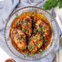 Juicy baked chicken drumsticks with a savory glaze and fresh herbs in a glass baking dish.