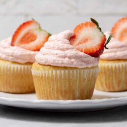 Fresh strawberry cupcakes with pink frosting and sliced strawberries on top.