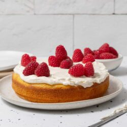 Fresh raspberry-topped sponge cake with whipped cream on a white plate.