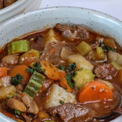 Hearty beef stew with vegetables in a rustic white bowl, perfect comfort food for cold days.