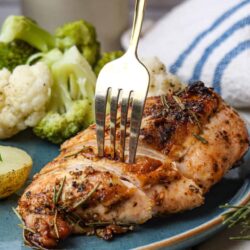Juicy roasted chicken breast with herbs served with steamed cauliflower and broccoli on a blue ceramic plate.