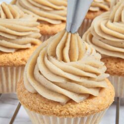 Cream cheese frosting piping on vanilla cupcakes with sprinkles of cinnamon, perfect for baking recipes.