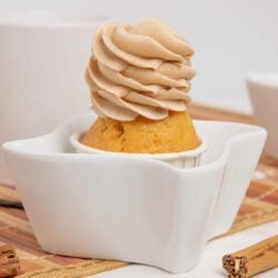 Creamy cinnamon frosting swirled on golden vanilla cupcake in white ceramic cupcake holder.