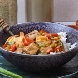 Savory chicken and vegetable stir-fry in a dark textured bowl, served with rice.