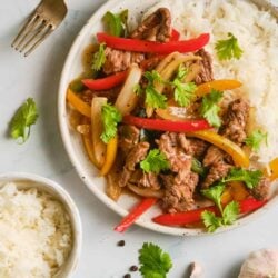 Savory beef stir-fry with colorful bell peppers and rice on a white plate.