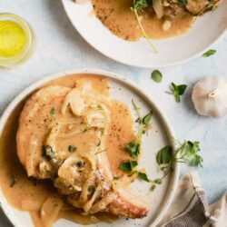 Juicy pork chops with creamy garlic sauce on white plates, garnished with fresh herbs. Perfect comfort food for dinner or special occasions.