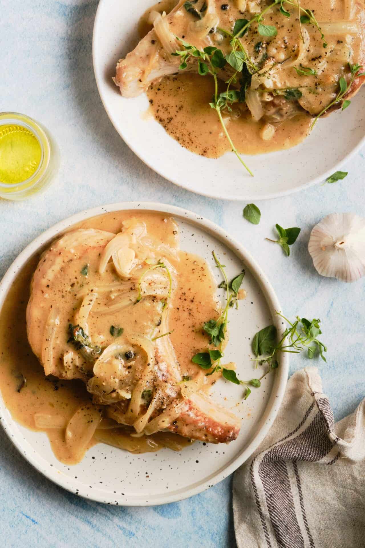 Juicy pork chops with creamy garlic sauce on white plates, garnished with fresh herbs. Perfect comfort food for dinner or special occasions.