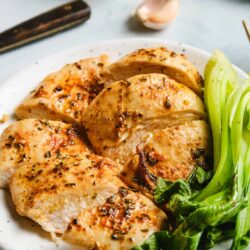 Juicy roasted chicken breast with herbs served with fresh celery stalks on a white plate.