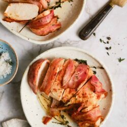 Succulent roasted chicken breasts wrapped in bacon garnished with fresh herbs for a flavorful meal.