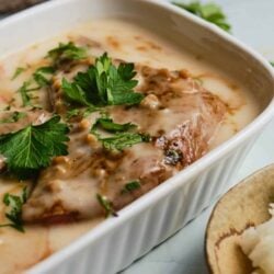 Creamy chicken pot pie with herbs and melted cheese in a white baking dish.