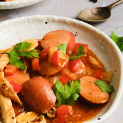 Savory sausage and vegetable stew in a rustic bowl, topped with fresh herbs.