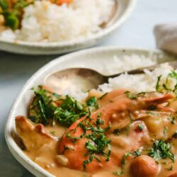 Creamy chicken and mushroom stew in white ceramic dish with chopped herbs.