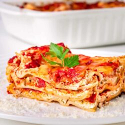 Oven-baked lasagna with cheese and tomato sauce on white plate.