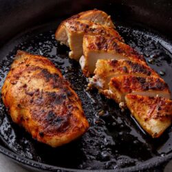 Juicy, crispy roasted chicken breast in cast iron skillet with golden crust and tender meat.