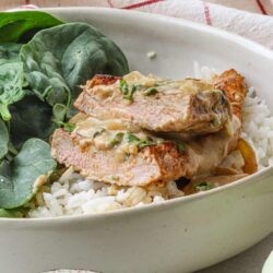 Juicy baked chicken breast with mushroom gravy served over rice, garnished with herbs.