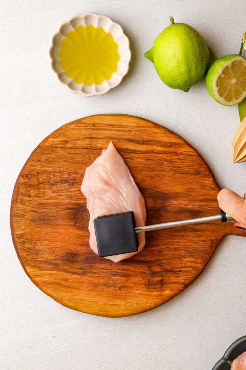 Fresh raw chicken breast on wooden cutting board with limes and lemon in the background for healthy recipes.